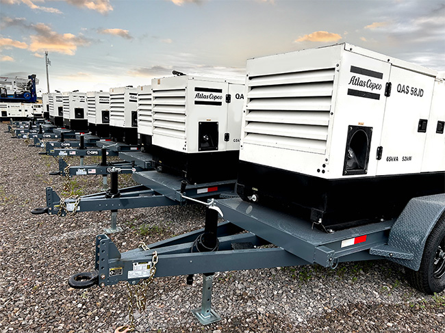 A row of towable industrial rental generators against a partly cloudy sunset sky.