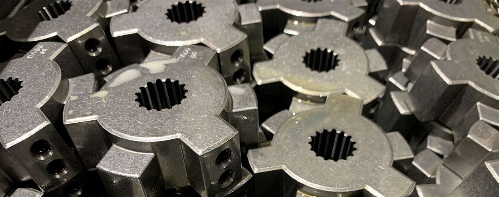 Close-up view of metallic power transmission components stacked together, showcasing precise machining with splined inner sections and holes for fastening. The parts have a polished, industrial finish, highlighting their durability and precision for heavy-duty applications.