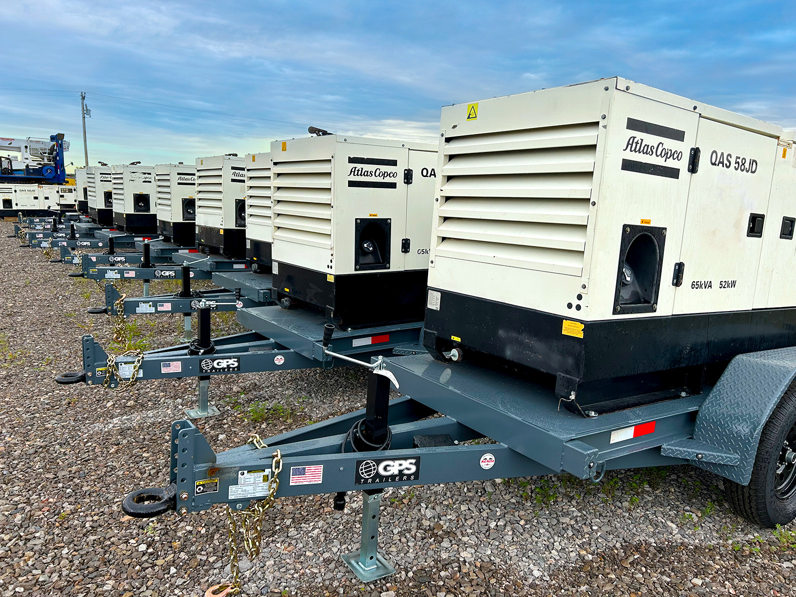 A row of towable industrial rental generators against a partly cloudy sky.