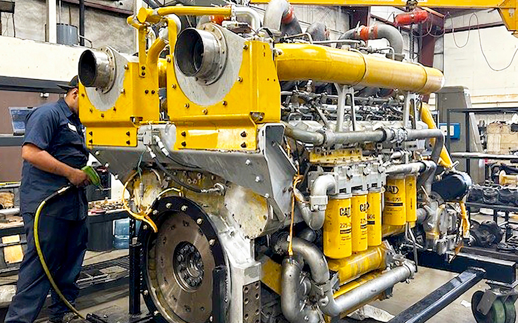 A technician performs maintenance on a large, industrial off-highway engine with a yellow and silver exterior.